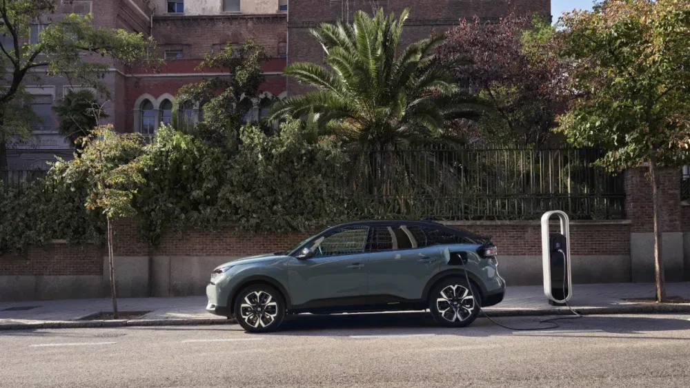 Zijaanzicht van de Citroën ë-C4, geparkeerd bij een laadpaal en aangesloten op de lader.